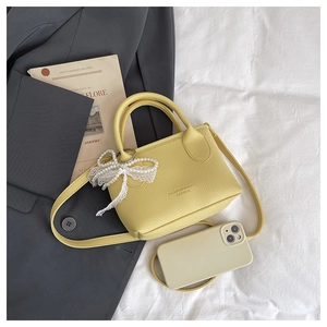 Close-up of litchi leather bag with pearl bow charm on a minimalist background
