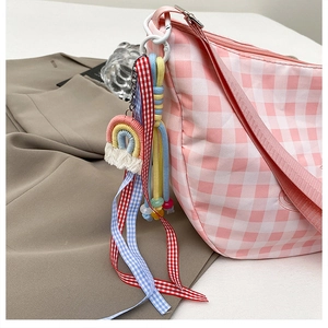 Detail of pink plaid canvas shoulder bag featuring crochet rainbow and ribbon charms