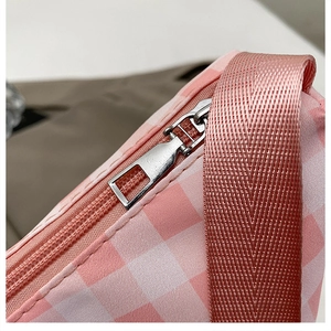 Macro shot of silver metal zipper and pink plaid fabric texture on the casual crossbody bag
