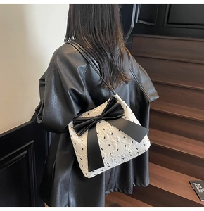 Détail du sac seau blanc matelassé avec grand nœud en cuir noir sur un mannequin
