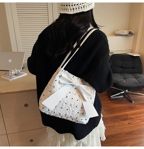 Close-up detail of white quilted handbag with black bow embroidery and large leather bow