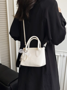 White minimalist pebble leather bucket bag with pearl charm shown on a crossbody model
