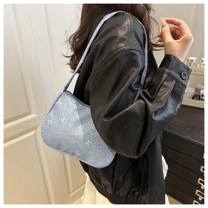Detailed view of light blue denim shoulder bag with colorful bow embroidery worn by model