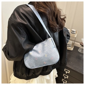 Detail of light blue denim baguette bag with colorful bow print worn on shoulder