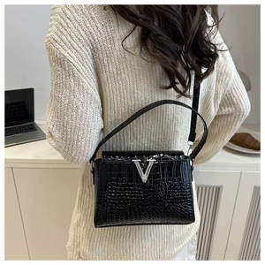 Detail of black crocodile texture handbag with silver V logo and slender strap in a lifestyle setting