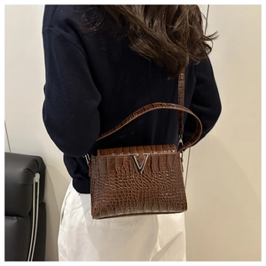 Detail of dark brown crocodile texture handbag with silver V-shaped metal hardware
