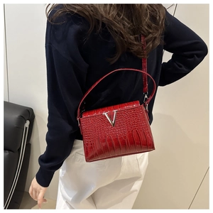 Model wearing a red crocodile-embossed shoulder bag with a silver V-shaped buckle