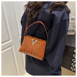 Brown crocodile texture crossbody bag with silver V buckle detail shown in lifestyle use