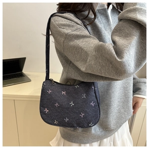 Detail of blue denim shoulder bag with colorful embroidered bows and metal zipper