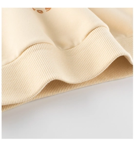 Detail of ribbed knit hem on a cream-colored children's sweatshirt with logo text