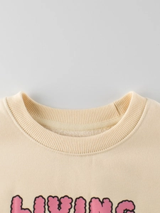 Close-up of cream crewneck sweatshirt for girls with pink Living bubble letter print