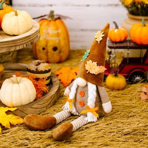 Detail of harvest gnome doll with maple leaf hat and long striped legs on autumn pumpkins