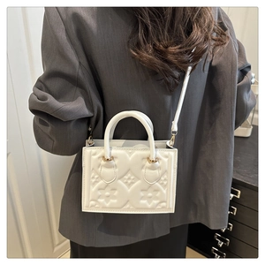 Detail view of white floral embossed small square bag on grey blazer for a modern look