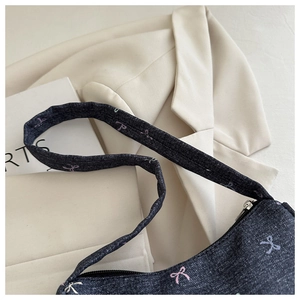 Close-up of dark blue denim shoulder bag featuring colorful bow patterns and zipper