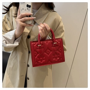 Detail of red leather handbag featuring embossed floral and star patterns with gold hardware