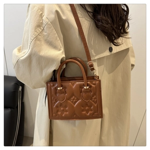 Detail of brown PU leather shoulder bag with floral embossed patterns on beige coat
