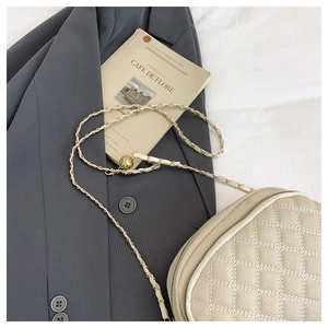 Detail of beige quilted crossbody bag with woven chain strap on a grey blazer