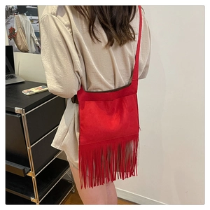 Close-up of red suede crossbody bag with long fringe tassels shown on model
