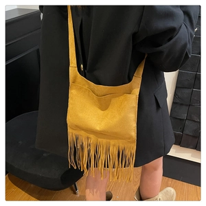 Detail of yellow suede fringe shoulder bag with bohemian tassels against black blazer