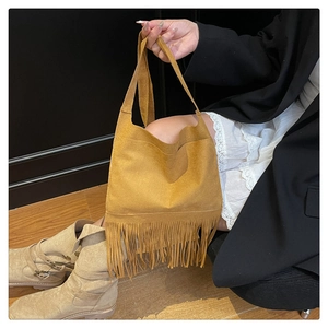 Detail of bohemian brown suede crossbody bag featuring long fringe tassels on white dress
