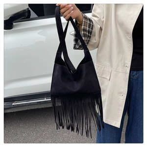 Outdoor close-up of a black matte suede handbag featuring long tassel fringe details