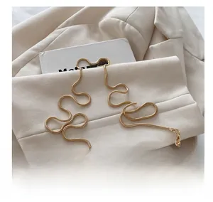 Détail d'une bandoulière chaîne serpent dorée posée sur un blazer beige et un livre