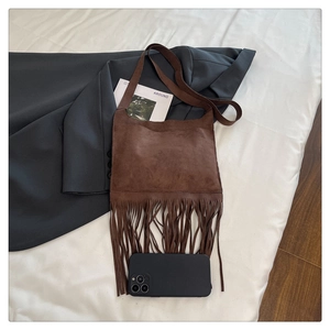 Macro shot of brown suede crossbody bag with long tassels and smartphone for size scale