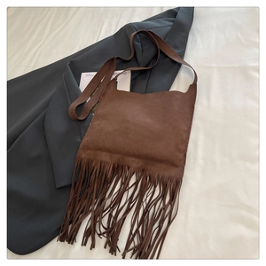 Close-up of brown suede crossbody bag featuring long bohemian tassels on white fabric