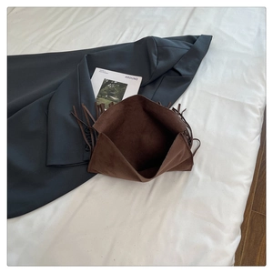Detail of vintage brown suede crossbody bag with fringe tassels on textured linen bedding