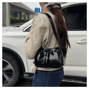 Close-up of black glossy patent leather shoulder bag with gold metal ring and drawstring