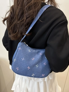 Deep blue denim shoulder bag with colorful bow embroidery shown on a model's shoulder