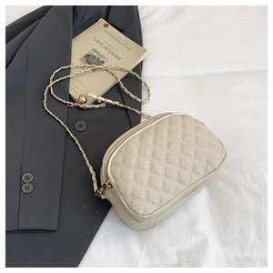 Close-up of cream quilted crossbody bag with gold chain strap on minimalist background