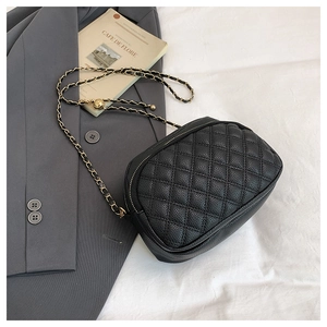 Detail of black quilted crossbody bag with gold chain strap on a blazer background