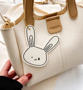 Close-up of cream PU leather tote bag with brown handles and fashion rabbit tag detail