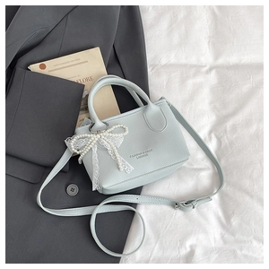 Close-up of light blue leather bucket bag with white lace bow and pearl charm detail