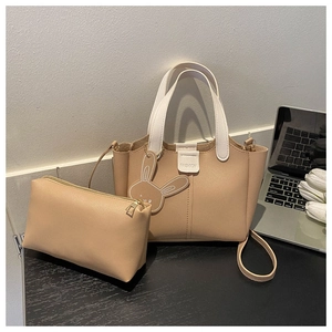 Detail of warm beige leather tote bag set with white contrast handles on wooden desk