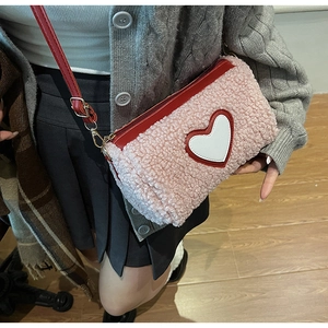 Detail of pink fleece crossbody bag with heart patch and red shoulder strap on a model