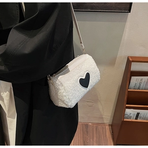 Detail of white faux shearling crossbody bag with black heart patch and gold buckle