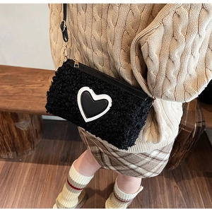 Detail of black plush handbag with heart patch and adjustable metal shoulder strap buckle