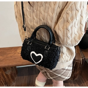 Détail du sac bandoulière en peluche noire avec écusson cœur et poignées en cuir élégantes