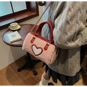 Close-up of pink fleece cylinder bag with white heart patch and red leather handle