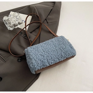 Close-up of light blue plush fleece handbag with brown leather base on a grey blazer