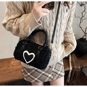 Detail of black faux shearling cylinder bag with white heart patch and leather handles