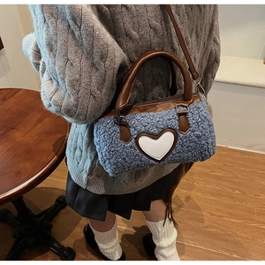 Détail du sac cylindrique en peluche bleue avec cœur en cuir blanc et anses marron