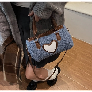 Detailed view of plush blue cylindrical handbag with white leather heart and brown strap