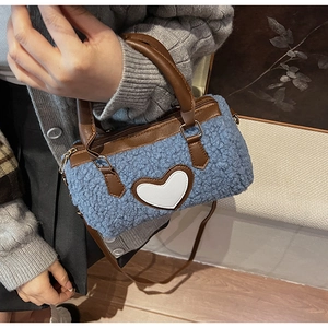 Detail of blue faux fur barrel bag featuring a white heart patch and brown leather handles