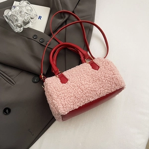 Détail d'un sac Boston en peluche rose avec lanières en cuir rouge sur blazer