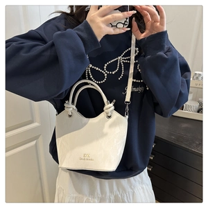 Detailed view of white bucket bag with textured leather, knot handle and gold brand logo