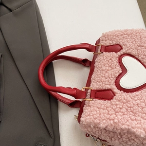 Détail du sac à main en peluche rose avec motif cœur blanc et poignées rouges