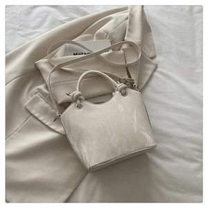 Detailed view of cream-colored handbag with marble texture on soft white fabric background